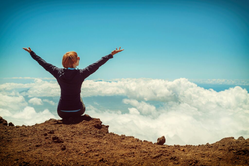 a woman sitting on a mountain with her arms raised